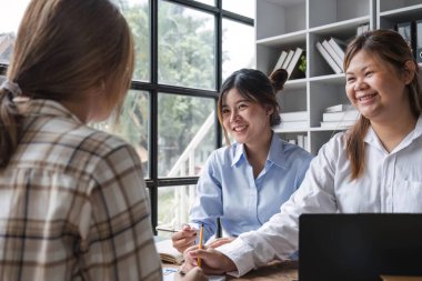 Asya Koleji öğrencilerinden oluşan gruplar dizüstü bilgisayar, tablet kullanıyor, not defterleri ile birlikte ders çalışıyorlar sınıftaki pencerelerin yakınındaki raporlar için belgeler hazırlıyorlar. Okul ödevi için iyi çalışmalar.