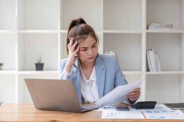 Kafası karışmış Asyalı kadın bilgisayar ekranına bakarak problemleri nasıl çözeceğini çok düşünüyor. Ciddi Asyalı iş kadını ofiste zor bilgisayarları çözmeye odaklanmış..