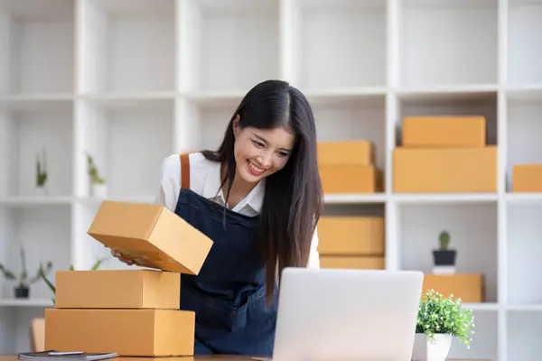 stock image Portrait business woman smile and use laptop checking information on parcel shipping box before send to customer. Entrepreneur small business working at home. SME business online marketing..