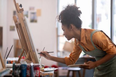 Stüdyosunda büyük bir zevkle çeşitli sanat projeleri üzerinde çalışan Afrikalı bir kadın ressamın portresi..