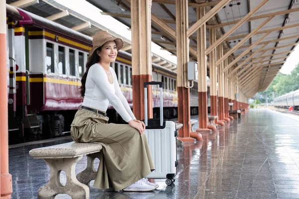 İstasyonda tren beklerken akıllı telefonunu kullanan Asyalı genç bir gezgin..