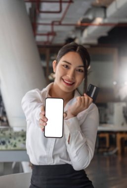 Güzel Asyalı kadın elinde akıllı telefon kopyası boş ekran ve kredi kartını gösteriyor..