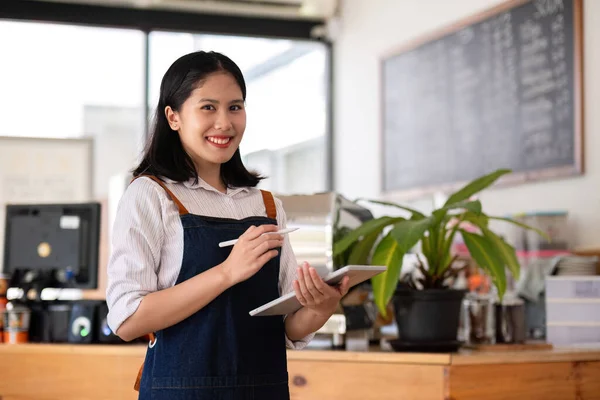 Opening a small business, A Happy Asian woman in an apron standing near a bar counter coffee shop, Small business owner, restaurant, barista, cafe, Online, SME, entrepreneur, and seller concept.