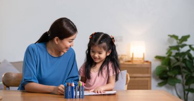 Genç bir aile boş zamanlarını evdeki oturma odasında geçirir. Anne ve küçük kızı pastel boyalarla resim çiziyor, mutlu bir şekilde gülümsüyor...