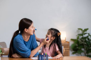 Genç bir aile boş zamanlarını evdeki oturma odasında geçirir. Anne ve küçük kızı pastel boyalarla resim çiziyor, mutlu bir şekilde gülümsüyor...