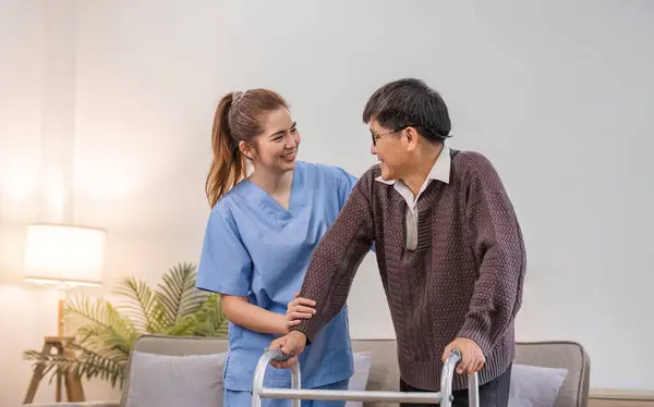 young asian female nurse care giver helping asian senior old man with mobility walker in living area of nursing home senior daycare center. Nurse take care elderly patient with cheerful concentrate.