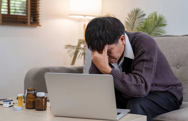 An elderly man with a headache is studying information about a medicine before taking it. Stressed elderly man Find drug information on your laptop.