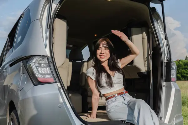 Young Asian woman sitting in the back of a car on an outdoor vacation. where the weather is clear Have fun traveling on holiday..