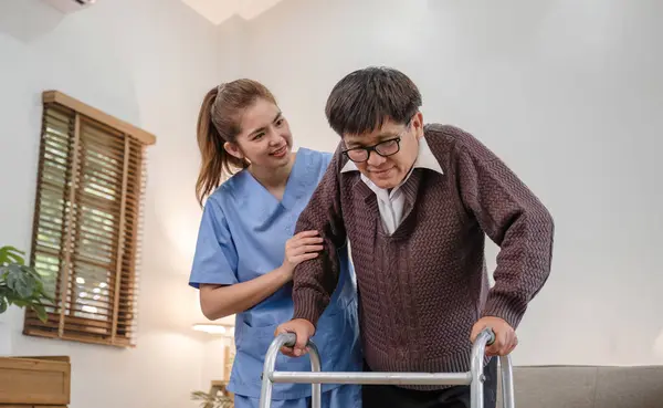 young asian female nurse care giver helping asian senior old man with mobility walker in living area of nursing home senior daycare center. Nurse take care elderly patient with cheerful concentrate.