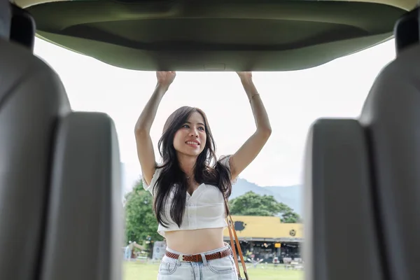 A beautiful young woman, sightseeing in nature, traveling by car on vacation, is closing the back door of the car to store things used in the travel trip. Traveling by private car.