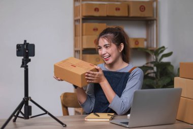 Telefonunda Asyalı blogcu ürünleri ve video kameraları inceler, internette satar ve ürünlerini sosyal medyada sergiler. ekommerce iş canlı yayın vlog yeni normal kavram.
