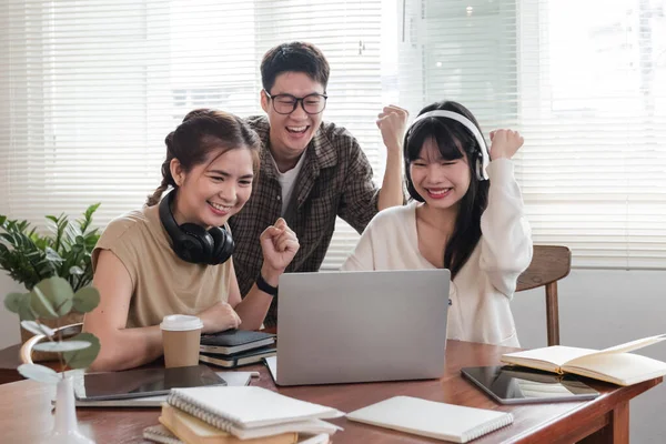 stock image A group of cheerful young university students are looking at a laptop screen and showing their fists, celebrating a good news together while sitting in a cafe..