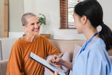 Kadın bir hemşire sağlık muayenesi bilgilerini toplayan bir belge tutar ve oturma odasında 60 'lı yaşlarda bir kişinin sağlık muayenesini tavsiye eder.