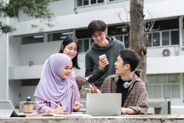Üniversitede aralarında Müslüman ve Asyalı öğrencilerin de yer aldığı çok ırklı bir öğrenci grubu kampüs molasında banklarda oturuyordu. Birlikte kitap okuyun ya da sınavlara çalışın...