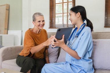 Genç hemşire sağlık muayenesi verilerini toplamak için bir tablet tutuyor ve 60 yaşındaki yaşlılara sağlık muayenesi öneriyor.