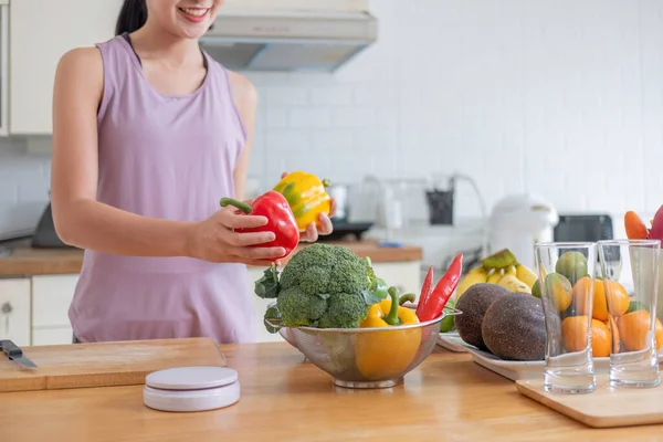 happy young woman cooking healthy vegetarian food at home. Fit smiling housewife or fitness coach in sportswear chopping peppers while making vegetable salad rich in vitamins.