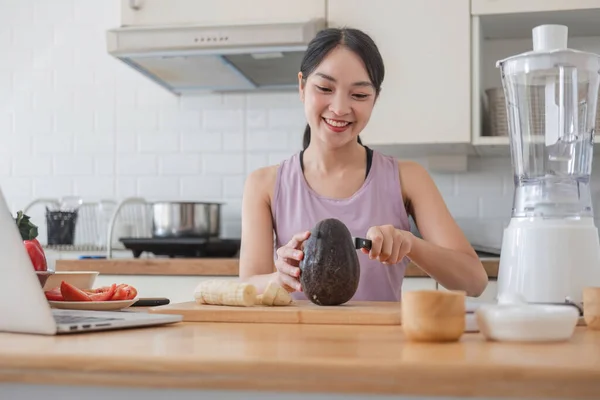 beautiful and fit Asian woman in gym clothes cutting an avocado and preparing her healthy breakfast in the kitchen before going to the gym