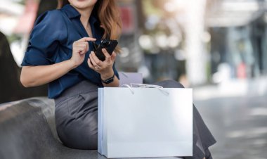 Akıllı telefonunu kullanan neşeli ve güzel Asyalı genç bayan alışveriş merkezinden alışveriş yaparken indirimli satışları kontrol ediyor...