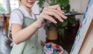 Resim stüdyosunda fırçayı tuvale boyayan mutlu Asyalı genç bir kadının resmini yakın çekim. Sanat atölyesi dersinde...