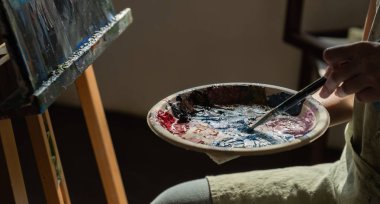 Kadın ressamın palette akrilik boya karıştırdığı yakın plan fotoğraf. Resim odasında tuval var..
