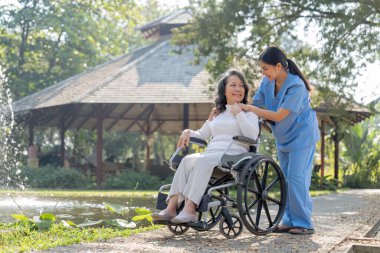 Üniformalı genç bir kadın ve tekerlekli sandalyedeki yaşlı bir hasta parkta takılıyor..