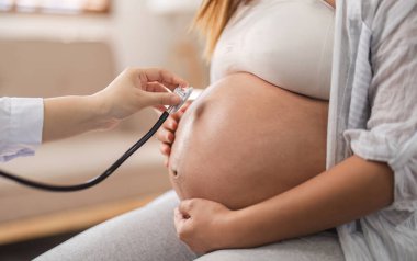 Steteskoplu bir kadın jinekoloğun eli rahmindeki bebeği ya da hamile bir kadının kalp atışlarını dinlemek için steteskop kullanıyor...