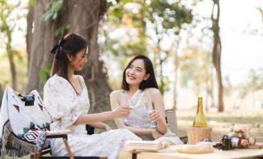 Gündelik giysiler ve yaz şapkaları içinde iki güzel LGBT 'li genç kadın dışarıda piknik yapıyor pozitif modelin önünde oturmuş meyve ve peynir yiyor ve selfie çekiyor. LGBT kavramı.