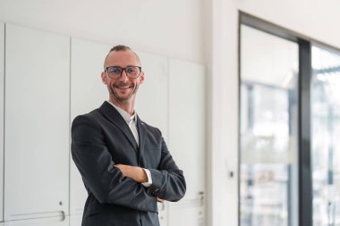 Çekici genç bir iş adamının portresi başarılı bir işletmeci kollarını ofisinde kavuşturup yüzünde mutlu bir gülümsemeyle durur...