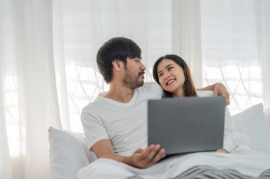 Evde yatarken dizüstü bilgisayar kullanan mutlu genç bir çiftin fotoğrafı...