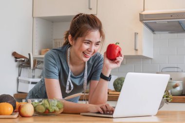 Egzersiz kıyafetleri içinde güzel genç bir kadın evde güzel bir mutfakta eğleniyor. Laptopunu vejetaryen meyve salatası sosu, meyve suyu ya da sağlıklı meyve suyu hazırlamak için kullanıyorsun...
