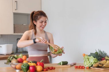 Genç atletik kadın, modern bir mutfakta sağlıklı bir organik sebze salatası hazırlıyor...