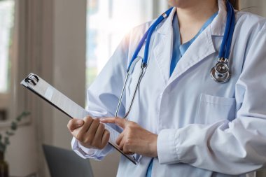 Elinde bilgi ve hasta bakım belgeleriyle gülümseyen kadın doktor. Ve hastanedeki doktor ofisinde steteskop..