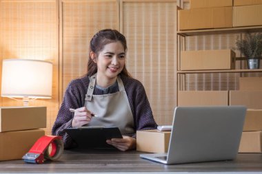 Startup small business entrepreneur SME, asian woman packing cloth in box. Portrait young Asian small business owner home office, online sell marketing delivery, SME e-commerce telemarketing concept.