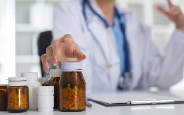 Kapatın, beyaz tıbbi üniformalı genç Asyalı doktor. Steteskopla laboratuvar bilgisayarı ve tablet kullanarak hastalara yönetime hazırlanan ilaçları düzenleyip sınıflandırıyor...