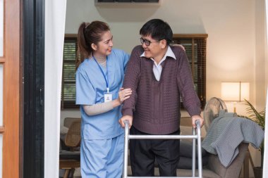 Asyalı kadın bakıcı, yaşlı bir adamın yürüteçle yürümesine yardım ediyor. Evde bir hemşire de ona yardım ediyor. Hemşire, huzurevindeki yaşlı bir hastaya yardım eder. Yaşlı bakımı ve sağlıklı yaşam tarzı.