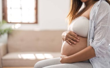 Hamilelik, dinlenme, rahatlama ve beklenti Mutlu hamile kadın kanepede oturuyor ve elini karnına koyuyor..