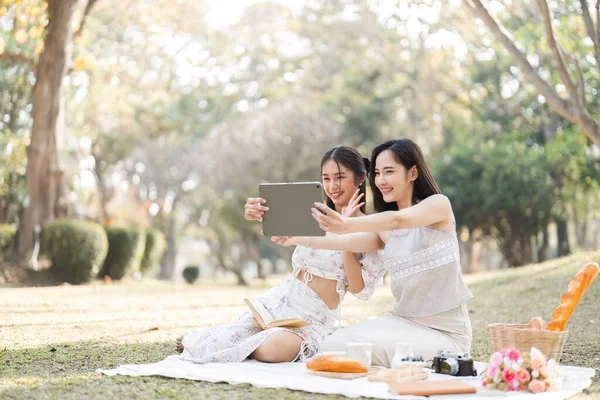 Two beautiful LGBT young women in casual clothes and summer hats Carefree woman having a picnic outside Positive model sitting on the grass eat fruit and cheese Take a selfie. LGBT concept.