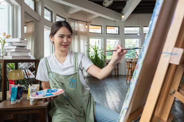 close up picture of happy young Asian woman painting brush on canvas in painting studio. In the art workshop class..
