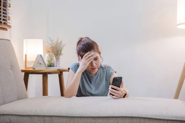 Sad woman reads bad news message Sitting lonely on the sofa in the living room Unhappy woman despairing over loss message on phone.