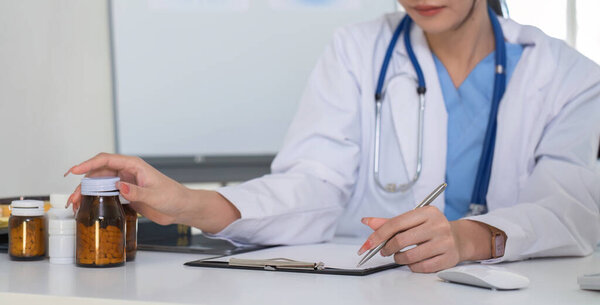 Крупным планом, молодой азиатский врач в белой медицинской форме со стетоскопом с использованием лабораторного компьютера и планшета для организации и классификации лекарств при подготовке к применению пациентам..