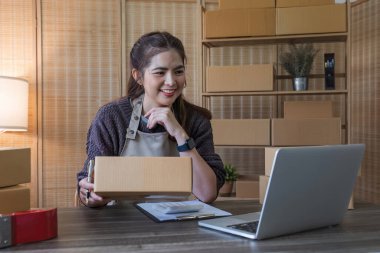 Startup small business entrepreneur SME, asian woman packing cloth in box. Portrait young Asian small business owner home office, online sell marketing delivery, SME e-commerce telemarketing concept.