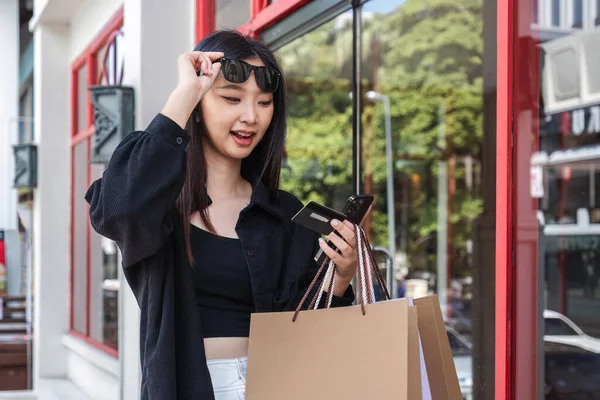 Portrait of attractive and playful Asian woman in casual clothes. Post a beautiful face showing off your credit card. View your collection on your mobile phone with Black Friday sales and discounts.