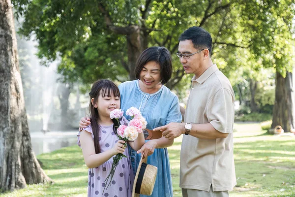 Kind-hearted Asian senior grandparent Warm and happy enjoying a stroll through the park with their adorable little granddaughter. On a clear day together lovely family.