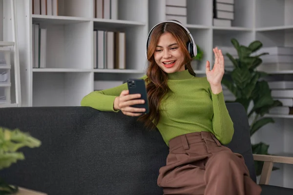 Happy Asian woman listening to music on mobile phone while sitting on sofa at home Relaxed smiling girl with headphones in the morning Its time to rest..