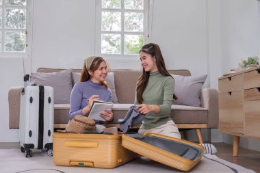 İki Asyalı bayan arkadaş tatile çıkmayı planlıyor, tatile çıkmadan önce bavullarını hazırlıyorlar...