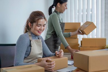 İki Asyalı girişimci kadın sipariş alır ve teslimat için müşteri siparişlerine göre kutuları işaretler...