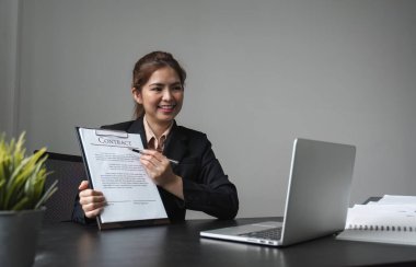 Genç bir iş kadını sözleşme imzalamayı ya da imzalamayı öneriyor. Bilgisayardaki çevrimiçi platformlar aracılığıyla iş imzalama.