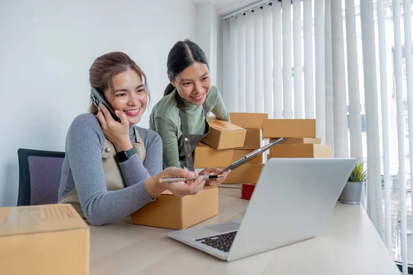 stock image Two Asian entrepreneur women take order and check boxes of products according to customer orders in preparation for delivery..