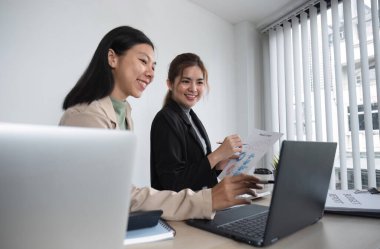 İki Asyalı iş kadını iş planlama fikirlerini tartışıyor. Ofisteki dizüstü bilgisayardaki grafik analizi.