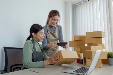 İki Asyalı girişimci kadın sipariş alır ve teslimat için müşteri siparişlerine göre kutuları işaretler...